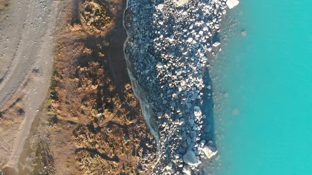 AERIAL: Zoom Out Over Glacial Lake And Rocky Coastline From A Drone