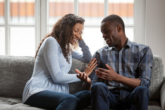 African American couple spending time together at home, sitting on couch, attractive woman and handsome man talking, having fun together, discuss, feeling happy, spend free time weekend together