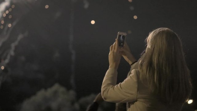 Girl shooting the salute on the smartphone. young girl photographs fireworks on the smartphone. City holiday, the birthday of the city.