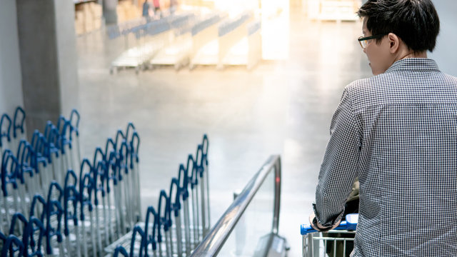 Young Asian man shopper holding shopping cart (trolley) on travelator (escalator) in supermarket or grocery store. Shopping lifestyle concept