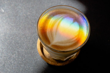 A prism dispersing sunlight splitting into a spectrum on coffee cup with heart shape latte art foam on black  table.