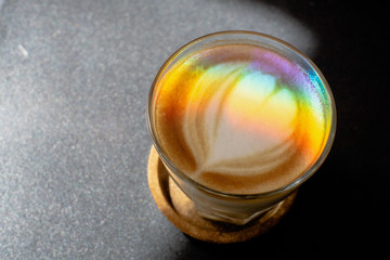A prism dispersing sunlight splitting into a spectrum on coffee cup with heart shape latte art foam on black  table,LGBT flag effect.