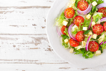 Fresh vegetable salad with tomatoes, lettuce, onion and cheese on white wooden background. Healthy vegetarian food. Top view