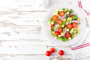 Fresh vegetable salad with tomatoes, lettuce, onion and cheese on white wooden background. Healthy vegetarian food. Top view