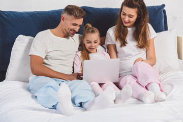 Family lying in bedroom in sleepwear with laptop