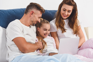 Obraz premium Smiling family lying in bedroom with laptop