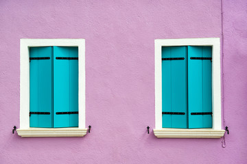 Beautiful windows with turquoise shutters on purple white wall. Colorful houses on Burano island near Venice, Italy