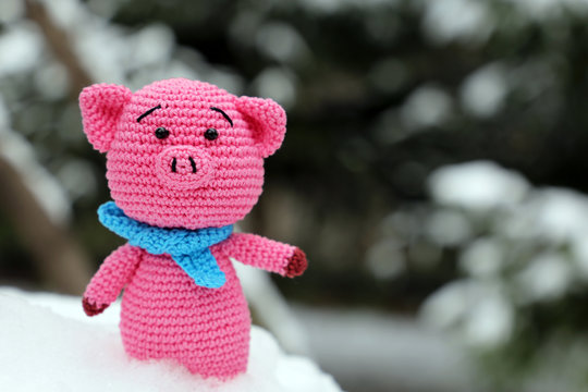 Knitted toy pig in the snow on background of Christmas trees. Festive card, Chinese New Year of Pig, Zodiac symbol 2019