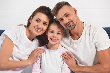 Fototapeta premium happy smiling parents hugging daughter in pajamas
