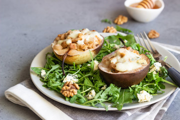 Obraz na płótnie Canvas Baked pears with gorgonzola, chicken, walnuts and mozzarella with arugula on a grey plate. Grey slate, stone or concrete table. Healthy salad or snack for Christmas or New Year. Copy space.