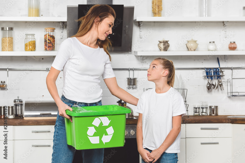 Wall mural mother holding green recycle box and looking at daughter