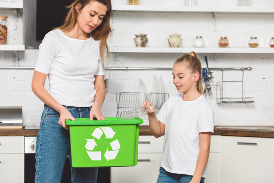 mother and daughter putting empty plastic bottles at green recycle box together