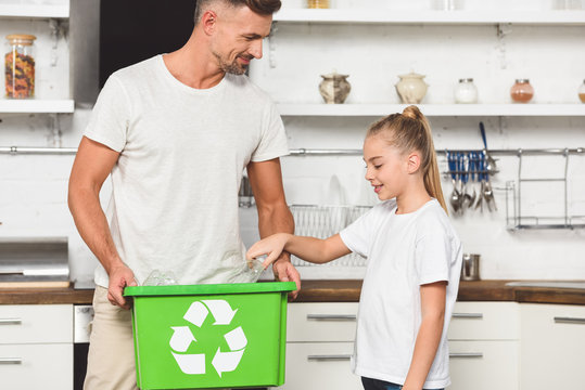 father and daughter putting empty plastic bottles at green recycle box together