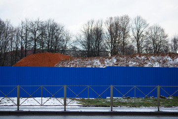 blue building fence and mountains of sand on the site of an industrial building - Powered by Adobe