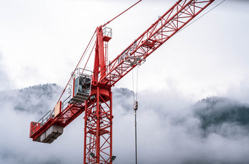 red construction crane in mountains in clouds