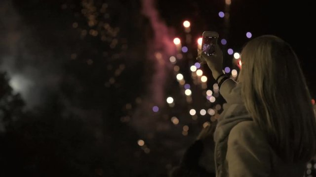 Girl shooting the salute on the smartphone. young girl photographs fireworks on the smartphone. City holiday, the birthday of the city.