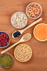 Various types of pulses, shot from above on a dark rustic wooden background with copy space. Red kidney, pinto, and black beans, lentils, chickpeas, soybeans, black-eyed peas
