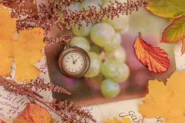 Nostalgia. A vintage pocket watch with autumn leaves and old postcards, shot from the top, toned image