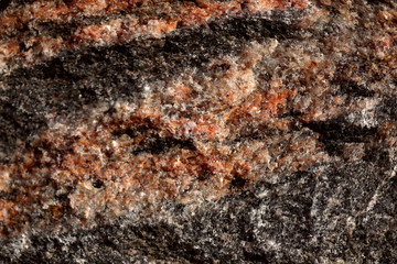 The structure of natural non-polished granite of black color with orange veins. Natural background, cropped shot, close-up. Concept of nature and production.