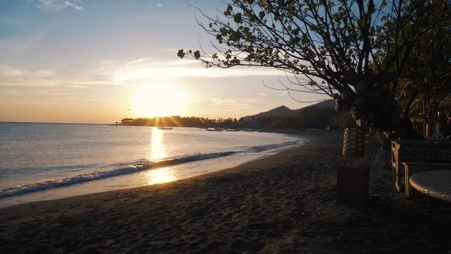 Peaceful beach landscape at sunrise, tree and table on right side, mountains in the back. Shot with Sony a7s and Atomos Ninja Flame on sunny summer morning.