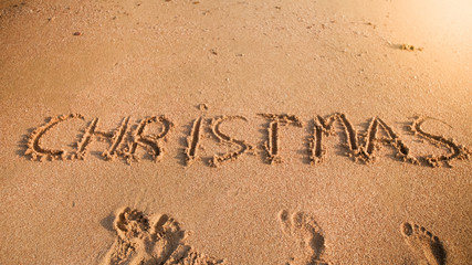Photo of word Christmas written on sand beach at ocean. Concept of winter holidays, New Year and tourism