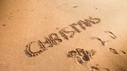 Closeup image of word Christmas inscripted on sandy beach. Footaprints on wet sand. Concept of winter holidays, New Year and tourism