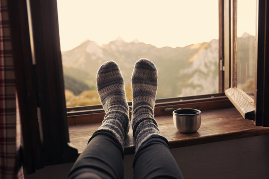 F&uuml;&szlig;e mit Wollsocken liegen auf einer Fensterbank mit Blick in die Berge
