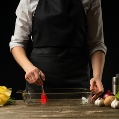 The chef lubricates a pot of oil for baking. On a black background, menu concept, cooking delicious food, healthy food.