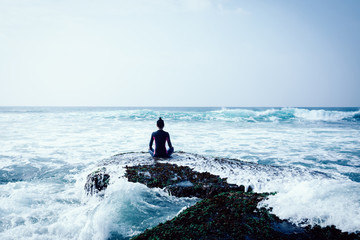 Woman meditation at the seaside cliff edge facing the coming strong sea waves