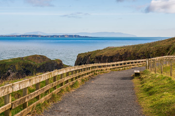 Fototapeta na wymiar Irish landscape in County Antrim, well known touristic destination in Northern Ireland. Road to Carrick-a-rede rope bridge on a sunny winter day. Bench with a view.