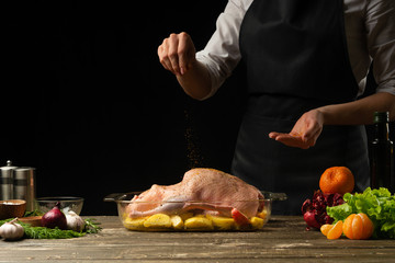 The chef seasoning the festive duck with potatoes for Christmas, New Year, Benefit Day. On a black background, menu, cooking delicious food, healthy food