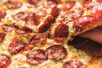 Hot pizza slice with melting cheese on a rustic wooden table.