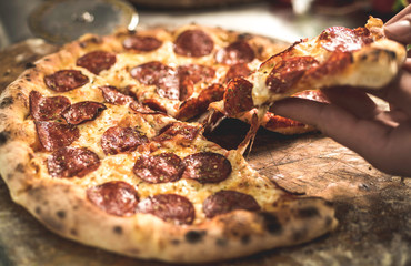 Hot pizza slice with melting cheese on a rustic wooden table.