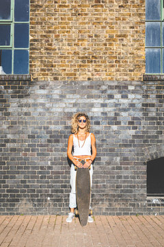 Young woman standing with skateboard at brick wall in the city