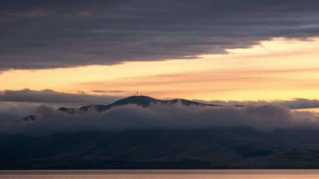 Time lapse of mountain surrounded by clouds during colorful sunset looking across Utah Lake.