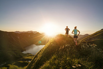 Man and woman running on mountain trail during sunrise
