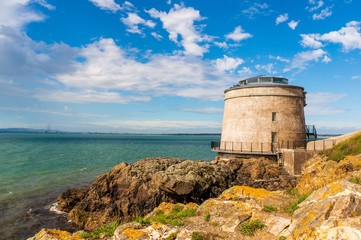Ireland landscape. Martello Tower under a beautiful blue sky with white clouds on the coast of...