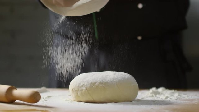 Close up shot of unrecognizable cook sieving flour on ball of dough lying on wooden table