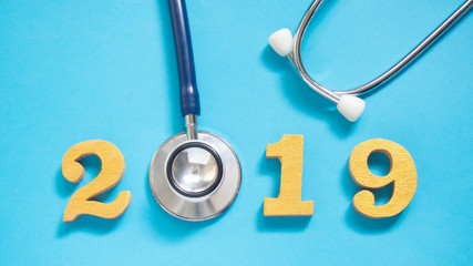 Stethoscope w/ 2019 gold wooden number on blue background. Happy New Year for healthcare and...