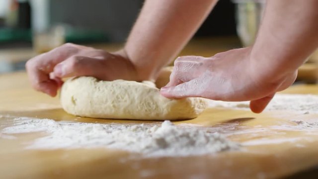 Close up shot of hands of unrecognizable male cook kneading dough on table