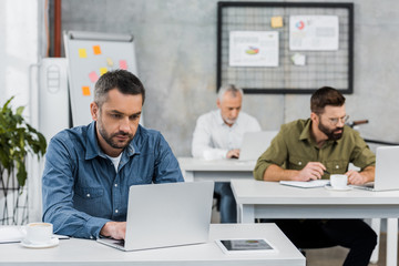 three handsome businessmen working at laptops in office