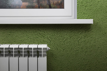 White heating radiator on the background of green wall under the window