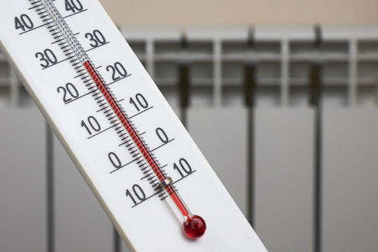 White alcohol room thermometer shows a comfortable temperature in the house against the background of a heating radiator.