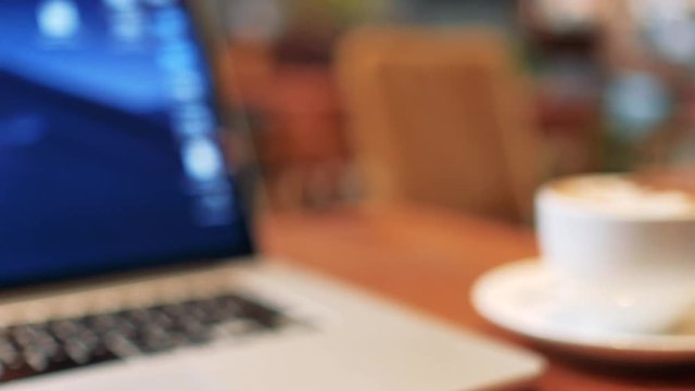 Blurry, defocus, out focus of a cup of cappuccino coffee with laptop on table. Royalty high quality free stock image of capuccino coffee with laptop for working in a coffee shop. Blur background
