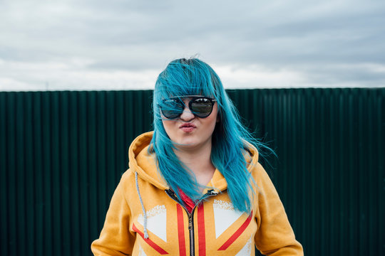 Portrait of young woman with dyed blue hair wearing sunglasses and hooded jacket