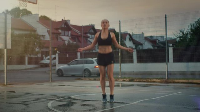 Beautiful Energetic Fitness Girl Skipping/Jumping Rope. She is Doing a Workout in a Fenced Outdoor Basketball Court. Afternoon Footage After Rain.