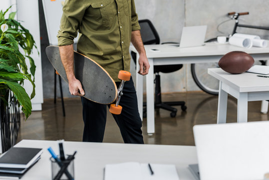 cropped image of businessman standing with longboard in office