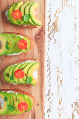Avocado sandwich on dark rye toast bread made with fresh sliced avocado, cream cheese, seeds and cherry on white wooden background
