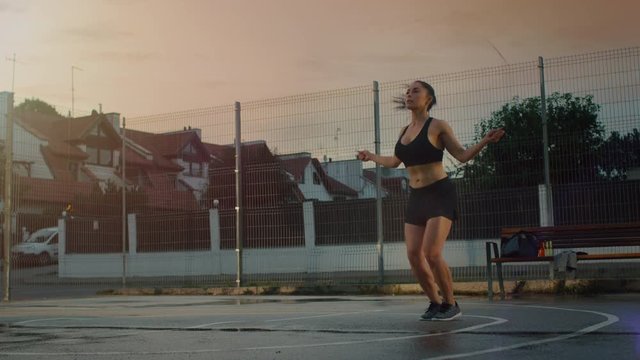Beautiful Energetic Fitness Girl Skipping/Jumping Rope. She is Doing a Workout in a Fenced Outdoor Basketball Court. Afternoon Footage After Rain in a Residential Neighborhood Area.