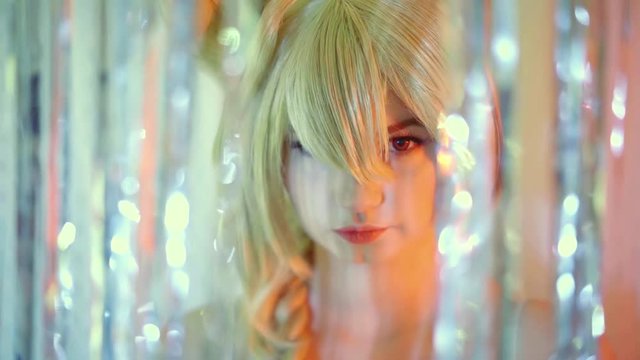 close-up portrait of a pretty girl in a wig and colored lenses in the eyes. she looks through a shiny holiday masher in the camera
